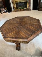 Angle view showing octagonal shape, dark wood finish, and carved sides of the table.
