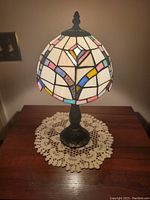 Image of vintage Tiffany-style lamp showing the stained glass hard plastic shade and ornate metal base, placed on wooden table over a crocheted doily.