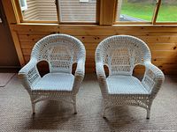Front view of two white wicker chairs showing the full seating and armrest design with open weave pattern.