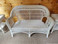 White wicker loveseat with detailed weaving and no cushions, showing structure and condition of wicker and legs.