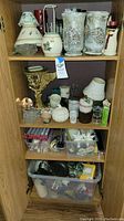 Shelves containing assorted candles, candle holders, and accessories organized in plastic bins and loose on wooden shelves