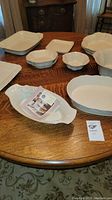 White stoneware dishes arranged on a table showing various sizes and shapes including large rectangular, square, oval, and round dishes with grapevine embossed patterns.