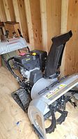 Side and angled view of the gray and black snow blower showing the engine, auger housing, and chute.