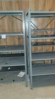 Photo showing two gray metal shelving units side by side, each with five shelves and some surface rust.