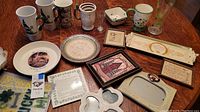 Photo of entire assortment of Irish-themed collectibles on a wood table including mugs, plates, framed pictures, and other ceramic items.