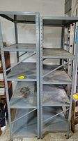 Front view of two connected metal shelving units showing multiple shelves with rust and dust buildup.