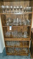 Full view of shelf unit holding multiple types of glassware including wine glasses, decanters, and bowls