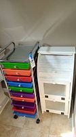 Photo showing two storage containers: colorful drawers on metal cart and white wooden cabinet