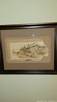 Framed vintage print showing a coastal village scene with cottages and a boat, housed in a dark wooden frame
