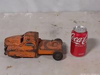 Side view of orange metal antique semi tractor toy next to a Coca-Cola can for size reference
