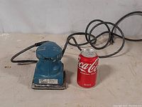Side-angle view of a blue electric finishing sander by Ohio Forge with power cord, placed next to a soda can for scale.
