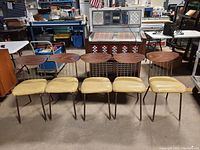 Five vintage metal framed dining chairs arranged in a row showing the wood veneer backrests and yellow vinyl seats.