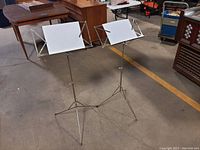 Two adjustable foldable tripod music stands shown fully extended with sheet holders open and ready for use.