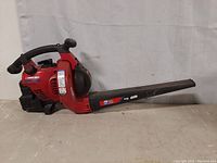 Side view of red and black handheld gas leaf blower with visible Troy-Bilt branding and elongated black nozzle