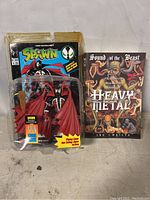 Photo showing Spawn action figure in packaging alongside Heavy Metal history book.