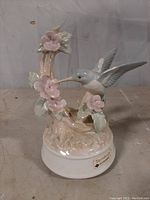 Front view of the hummingbird music box showing the hummingbird, flowers, and branch detail with the Otagiri Tenderly label on the base.