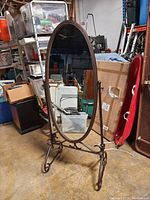 Full front view of the full size standing oval mirror showing antique brown metal frame and scrollwork base