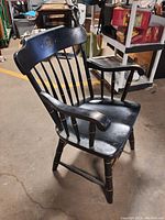 Side angle of the black Windsor armchair showing armrest, seat, legs, and logo on backrest; scratches and wear visible