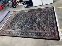 Full view of the oriental style rug showing black border and complex floral and paisley patterns on dark background.