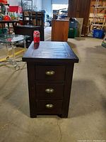 Side view of small dark wood end table with three drawers and brass cup handles, showing its height compared to a soda can.
