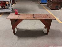 Front view of small rectangular wooden bench with a flat top surface and two legs with diagonal braces. Shows natural wood finish with some stains and wear marks.