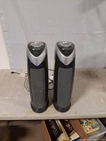 Front view of two GermGuardian tower air purifiers positioned side by side with visible front grilles and top control panel.