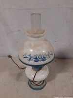 Front view of the vintage milk glass lamp showing blue floral and vine design, glass chimney and base.