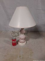 Front view of vintage pink milk glass lamp with white lampshade next to a soda can for scale.