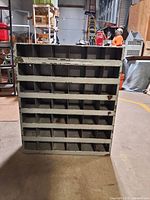 Front view of vintage metal parts bin shelving unit showing multiple rows of cubby compartments and surface wear.