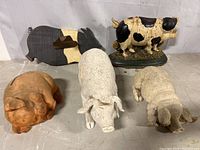 Front view of all five pig-themed decorative pieces arranged in a row on a gray surface against white background, showing variety of materials and textures