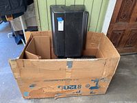 Photo of the boxed black plastic grill parts including the grill hood/lid and base parts inside a worn cardboard box