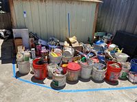 Wide view of large assortment of buckets and boxes filled with various tools, hardware, and home improvement materials outside a metal shed.