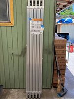 Folded scaffolding trestle and plank leaning against a green wall, packaging present