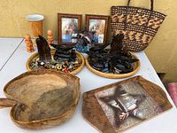Lot laid out on table showing two plaques with wooden carvings, wooden picture frames, wooden bowl, ceramic salt and pepper shakers, vase, keychains, and pen holders