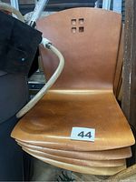 Stacked view of four light wooden chairs showing curved seats and backrests with square cutouts.