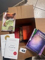 Box open showing assortment of books including 'The Easiest Keto Air Fryer Cookbook,' 'Emerging from the Darkness,' 'The Art of D'scaring,' and 'Implausible'.