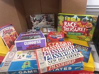 Photo showing eight vintage games arranged inside a cardboard box with clear titles including Password, Guinness World Records game, Annie card game, and Race to the Treasure!