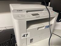 Front view of Canon multifunction printer showing model branding, paper tray, buttons, and control display
