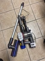 Dyson handheld vacuum with wand, battery, motorized roller brush and crevice tool laid on tiled floor.