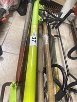 Photo showing long-handled garden tools with wooden shafts and metal ends including a bright green metal tool.