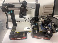 Two Kingroon branded 3D printers or parts side by side on a flat surface. One fully assembled, the other missing some components with exposed wiring.