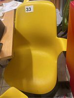 Single yellow molded plastic chair with armrests and curved backrest, positioned next to a wooden surface.