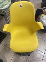 Yellow molded plastic chair with armrests and curved backrest, placed on tiled floor.