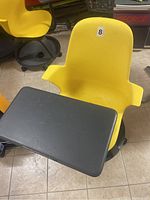 Close-up of yellow plastic chair showing attached black tray, base with wheels, and surface condition