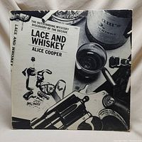 Front cover of the vinyl album showing guns, money, whiskey bottle and glass in black and white monochrome.