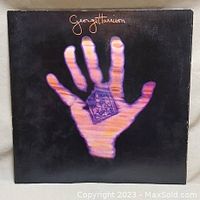 Front cover of the vinyl album showing a large purple hand holding a card on a black background with George Harrison's name