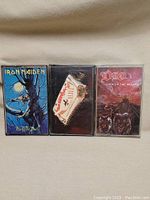 Front view of all three cassette tapes in their cases: Iron Maiden Fear of the Dark, Motorhead The Birthday Party, and Dio Lock up the Wolves.