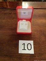 Pair of small stud earrings in a red jewelry box with white cushioned interior, photographed on a wooden surface with a lot number card '10'.