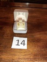 Pair of earrings in open grey velvet box with white holder, '14 KT. GOLD' printed, displayed on wooden surface with lot number card '14'
