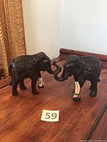 Two black resin elephant figurines facing each other, showing carved decorative patterns and white tusks on a wooden surface